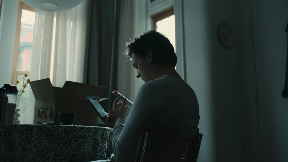 Jared at the window with a cigarette, an opened box beside him.