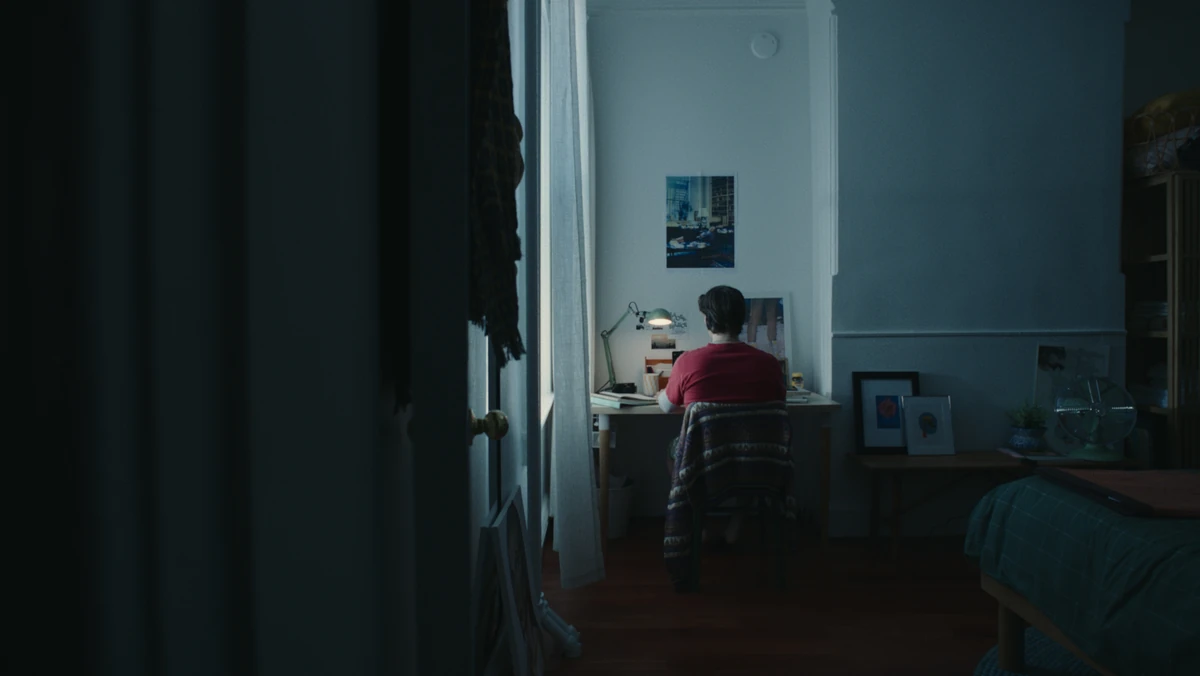 The apartment corridor at dusk, a figure at the desk beyond.